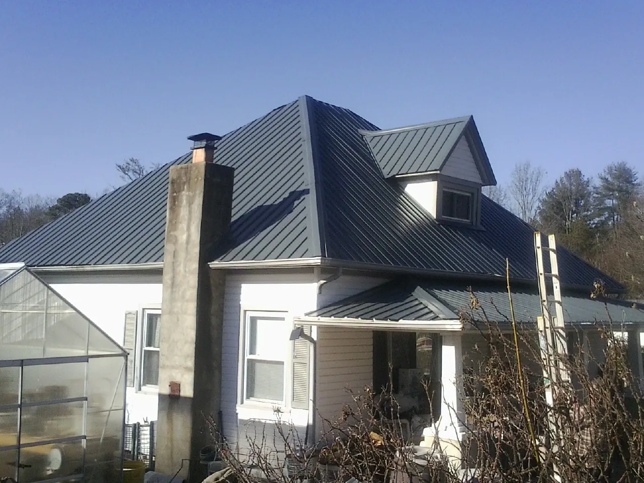 Dark blue standing seam metal roof on a white farmhouse with dormer — Slate & Tile Roof Repair by Roofing Brothers in Deland