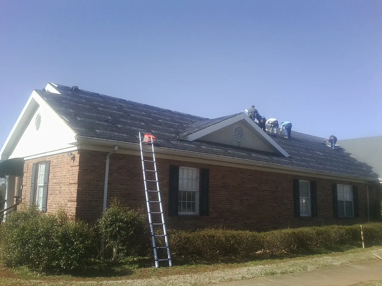 Crew tearing shingles off a brick ranch roof with a ladder set — Metal Roof Repair work by our crew in Deland