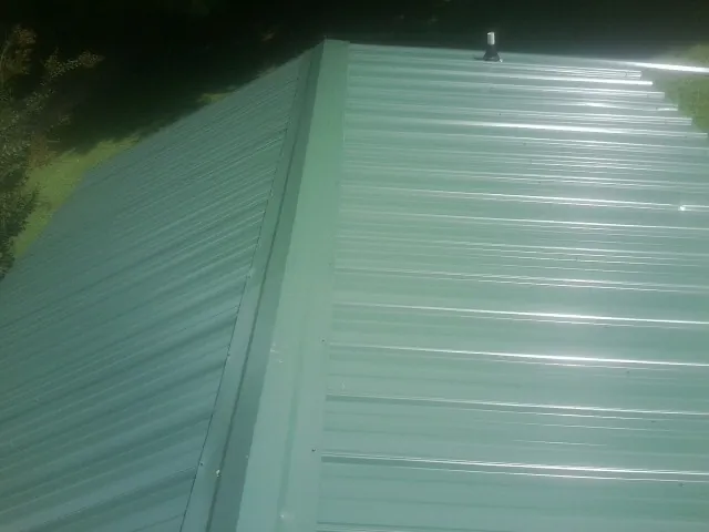 New green metal panels meeting at the ridge of a roof — Flat Roof Repair work by our crew in Deland