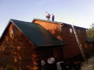 Crew on the ridge of a green metal roof on a two story log home in Deland