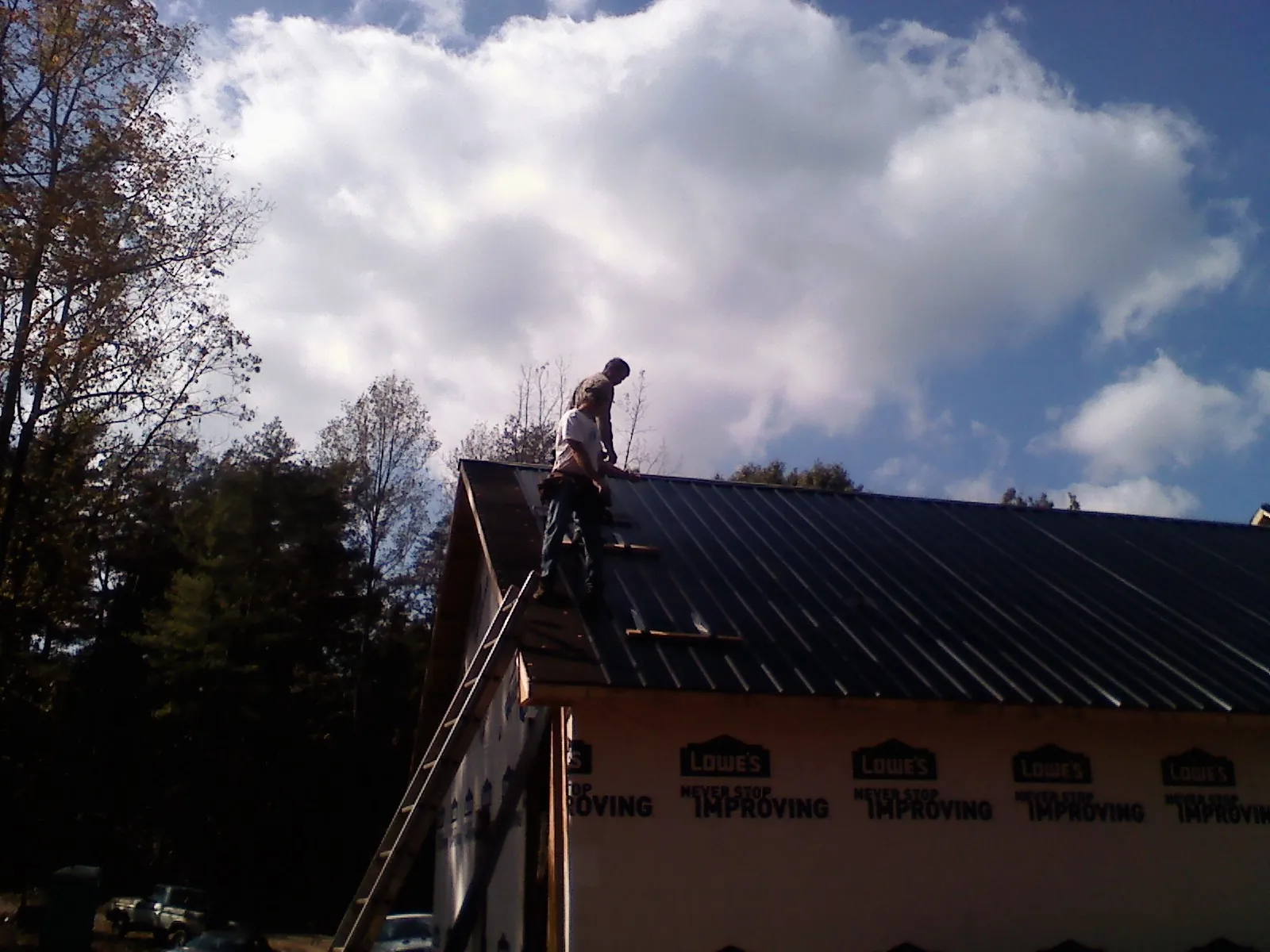 Roofer fastening dark metal panels high against a cloudy sky, from a Roof Inspection job in Deland