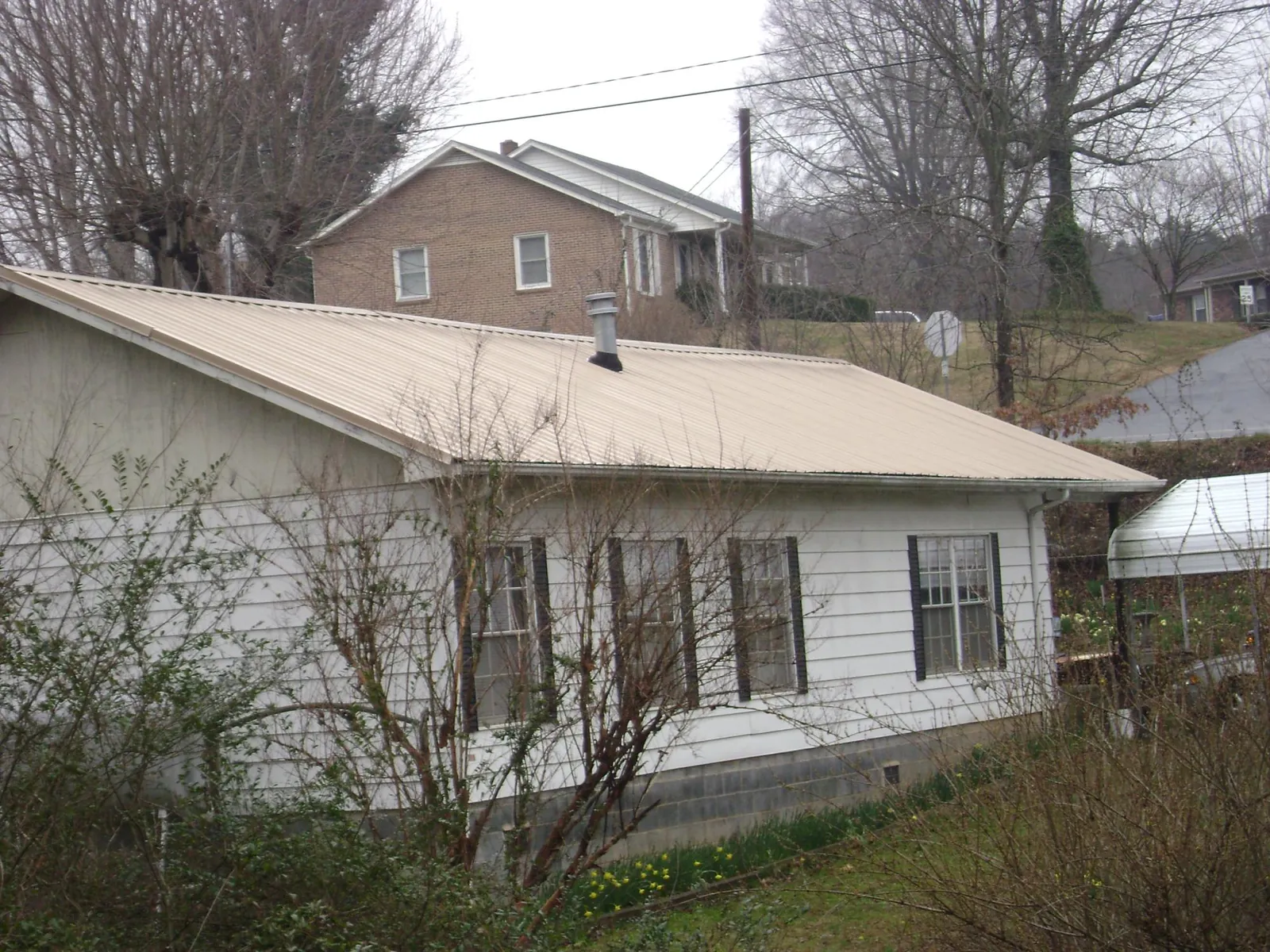 Tan metal roof on a white sided house set into a hillside — Commercial Roofing by Roofing Brothers in Deland